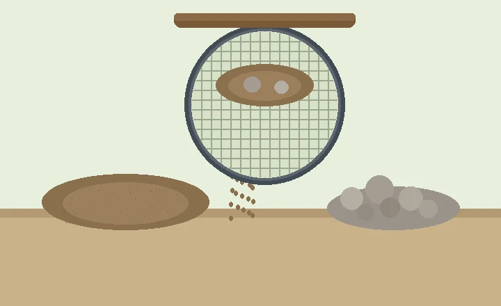 A round garden sieve with fine mesh held over a tray, screened soil falling through beside a pile of stones